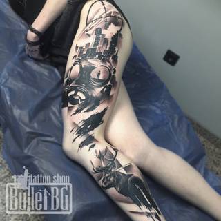 Czarno-biały tatuaż na całą nogę z motywami maski gazowej, miasta i jelenia.