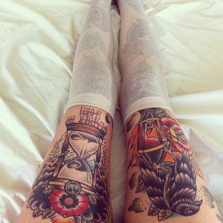 Kolorowe tatuaże na nogach + zakolanówki. Widzimy ptaka bez klatki, kwiat. Na drugiej nodze: zegar (klepsydre) i napis.