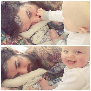 Mężczyzna z dużą ilością tatuaży i dziecko. Ma on napis na czole i przy policzku oraz wytatuowaną górną częśc ciała