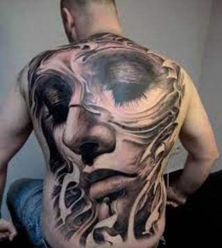 Niezwykły tatuaż na plecach mężczyzny. Jest to twarz kobiety z opuszczonymi w dół i pomalowanymi na ciemno oczami.