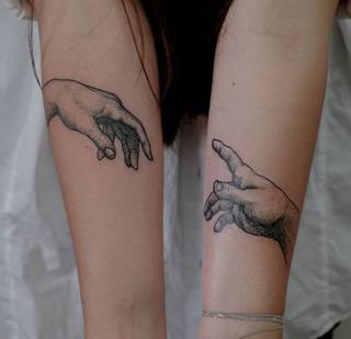 Stykające się dłonie Boga i Adama odwzorowane na przedramionach u dziewczyny.