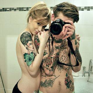 Wytatuowana para. Dziewczyna ma na ramieniu kolorową damę z ozdobą we włosach. Chłopak ma wytatuowaną głównie górną część ciała (niektóre w kolorze)